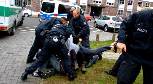Mehrere deutsche Polizisten, die gewaltsam gegen Protestierende vorgehen, die auf dem Boden liegen.
