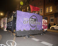 Demofront der Antifademo. Lilanes Transparent mit schwarzem Antifalogo und Stadt-Sillouette. "Antifa in die Offensive" steht darauf. Eine rote Fahne auf der "Gegen Nazis" steht wird dahinter geschwenkt.