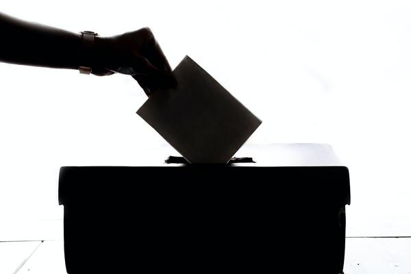 Eine Hand wirft einen Briefumschlag in eine Wahlurne. Das Bild ist schwarz/weiß.